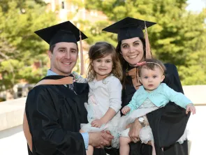 Two graduates of the MBA program pose in their graduation regalia with their children