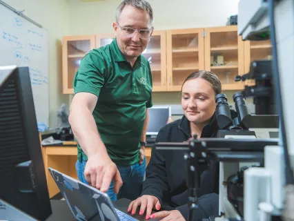 A male faculty member is pointing to a data point on a screen for a student