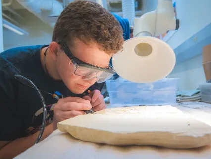 Male student working on a fossil specimen in lab