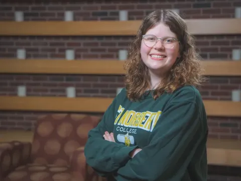 Female student standing in front of a brick wall with candles.