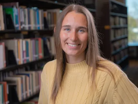 Female student in front of shelves of books in a library.