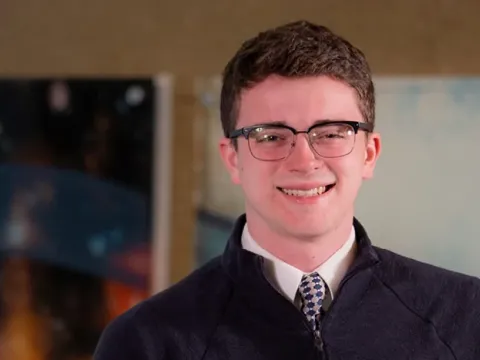 Male student stands in front of an art installation.