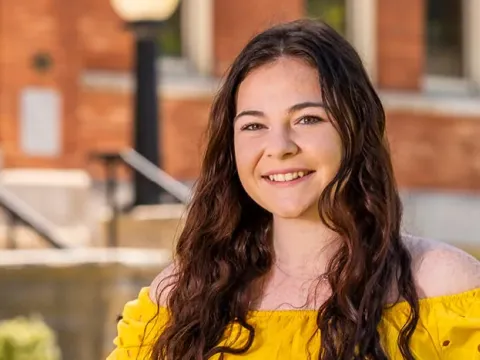 Female students stands outside in front of a brick building.