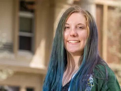 Female student standing outside in front of a brick building.