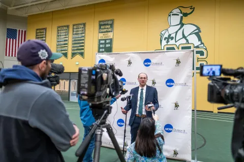 The athletic director talking to the media in front of a branded wall.