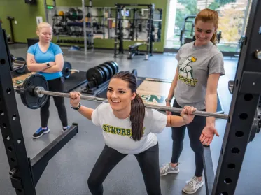 A student lifting weights while others spot them
